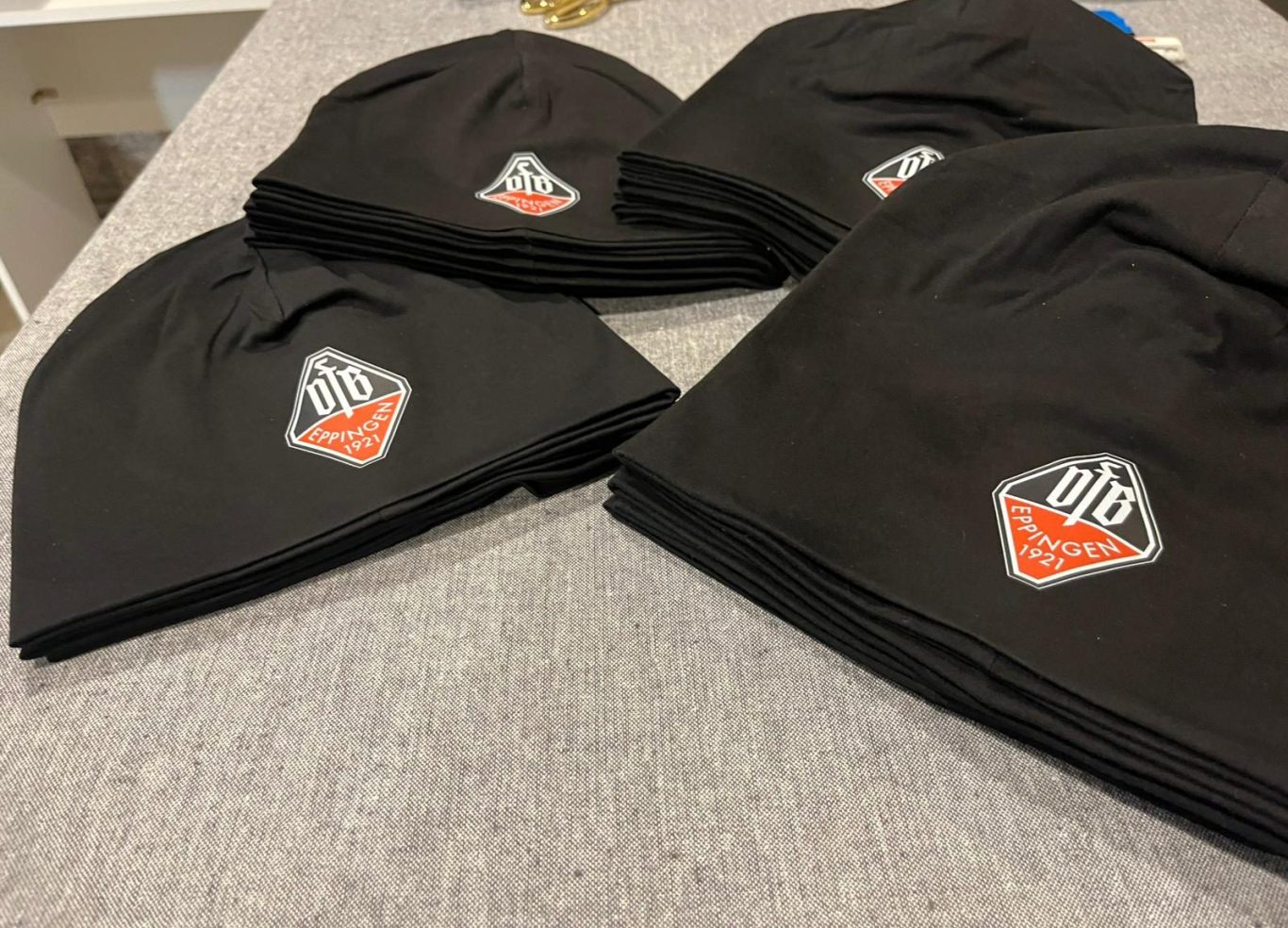 Schwarze Mützen mit einem farbigen Logo, auf einem flachen Untergrund angeordnet.